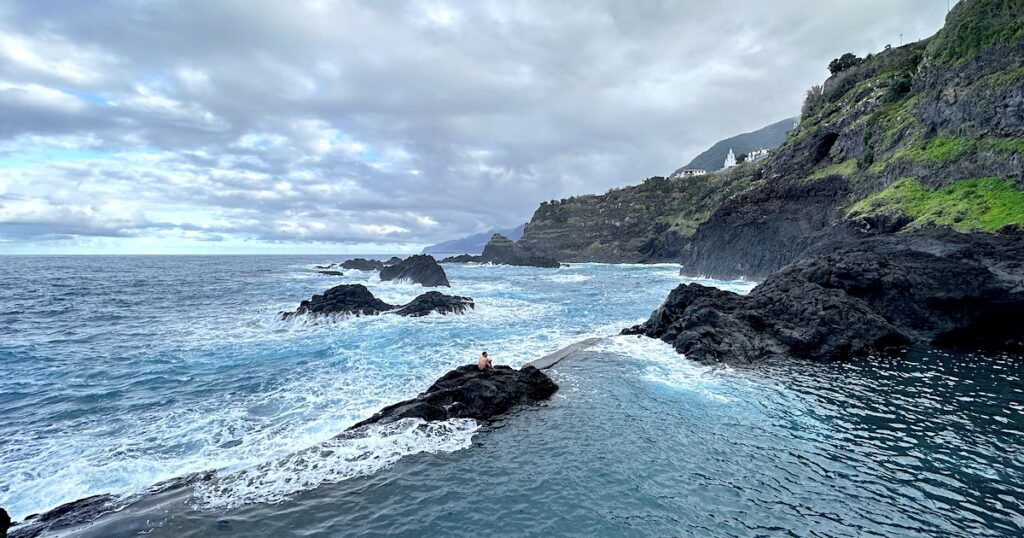 A man stands on a volcanic rock on the edge of the Seixal natural pools.