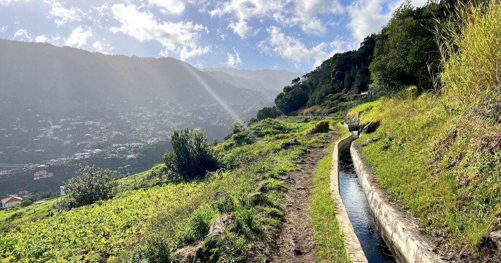 Clear water runs through Levada dos Maroços overlooking terracotta houses in a green valley.