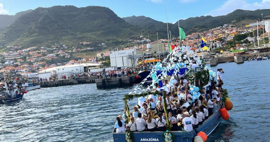 A large, blue boat decorated in balloons sails towards Caniçal port as part of the Caniçal fishing fiesta.