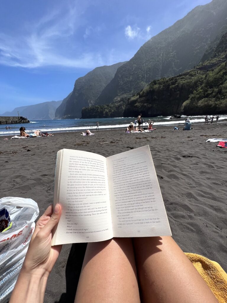A person reads a book at the black-sand Seixal Beach in Madeira.