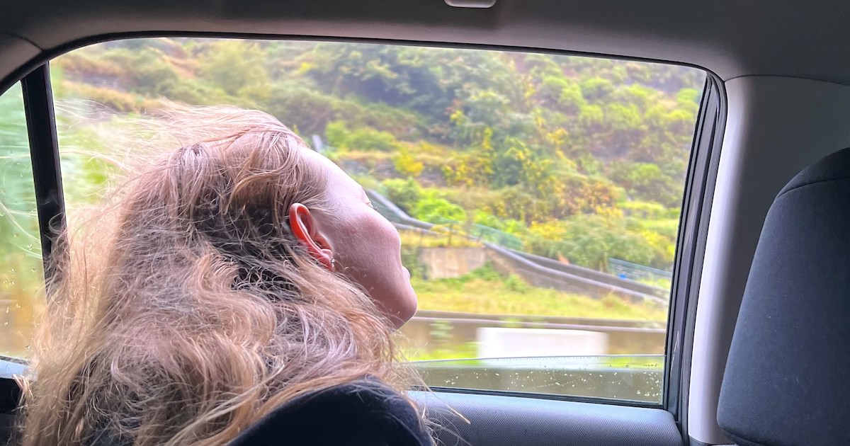 A woman gazes out at green slopes from a car in Madeira.