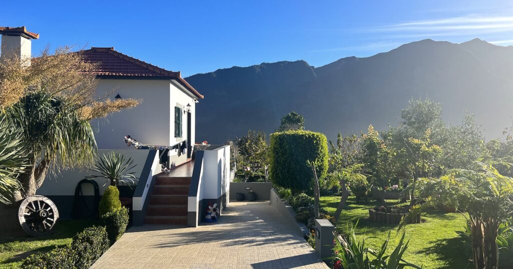 A white cottage next to landscaped gardens, with mountains in the background.