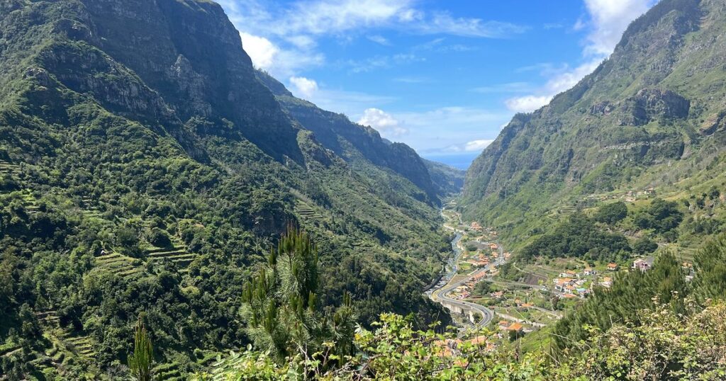 A winding road passes through a green valley with mountains in Madeira.