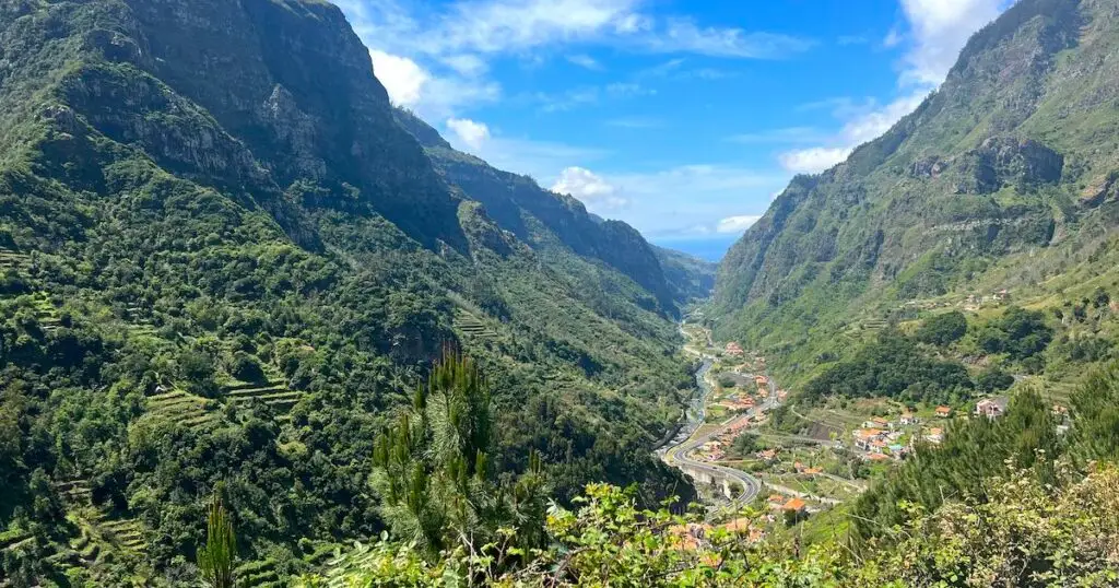 A winding road passes through a green valley with mountains in Madeira.