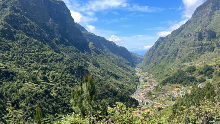 A winding road passes through a green valley with mountains in Madeira.