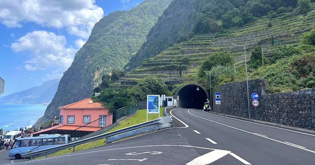 A main road goes into a tunnel through the steep, green north coast of Madeira.