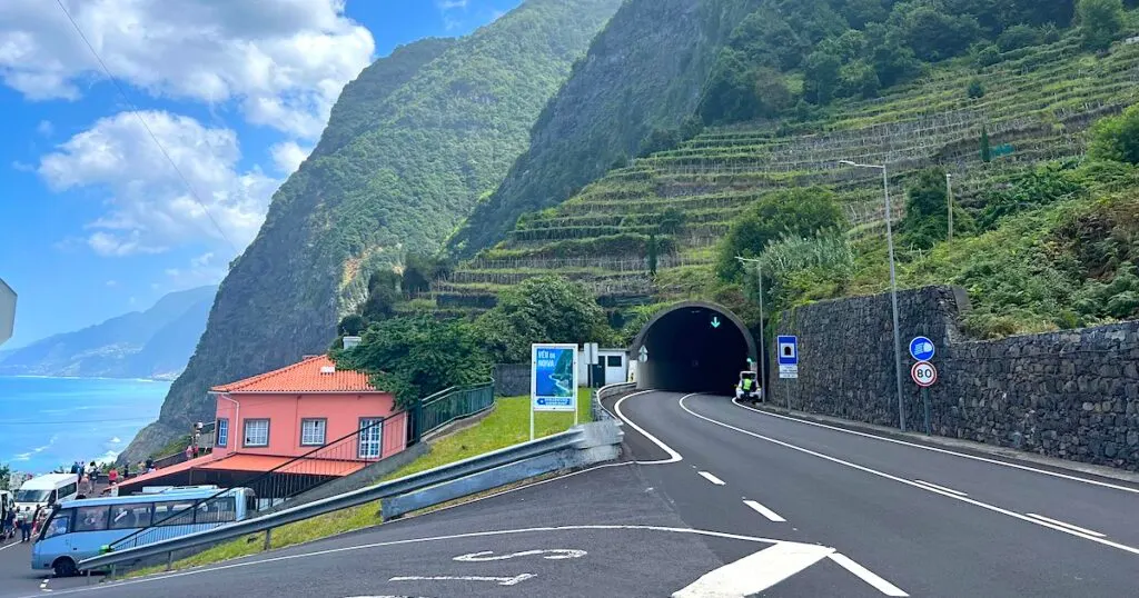 A main road goes into a tunnel through the steep, green north coast of Madeira.