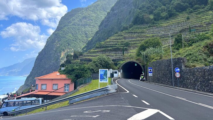A main road goes into a tunnel through the steep, green north coast of Madeira.