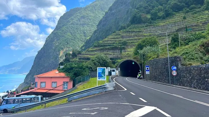 A main road goes into a tunnel through the steep, green north coast of Madeira.