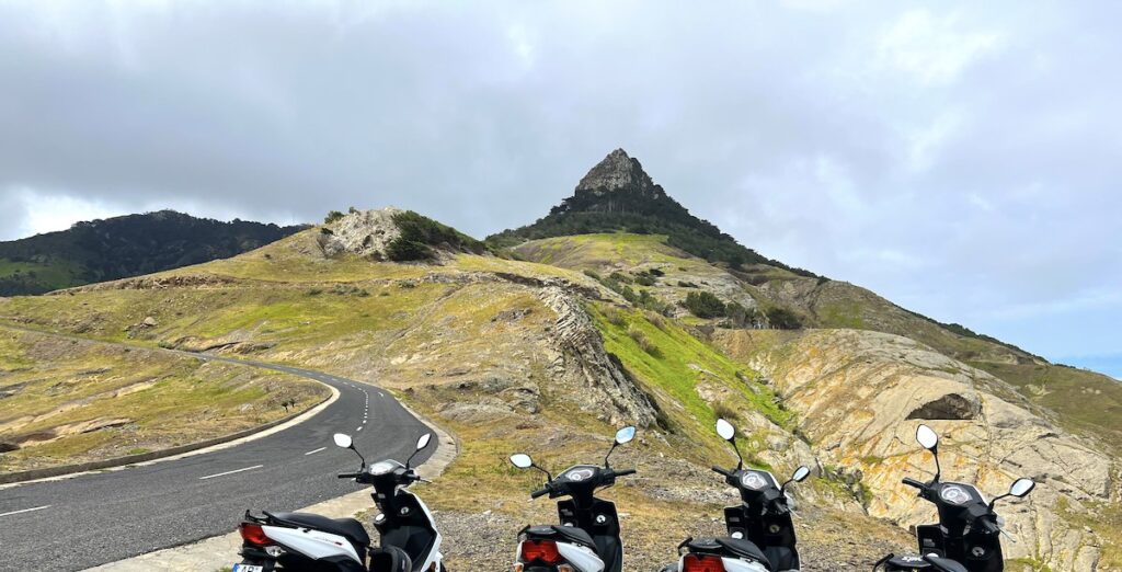 Four scooters parked on the side of a winding road next to a mountain in Porto Santo.