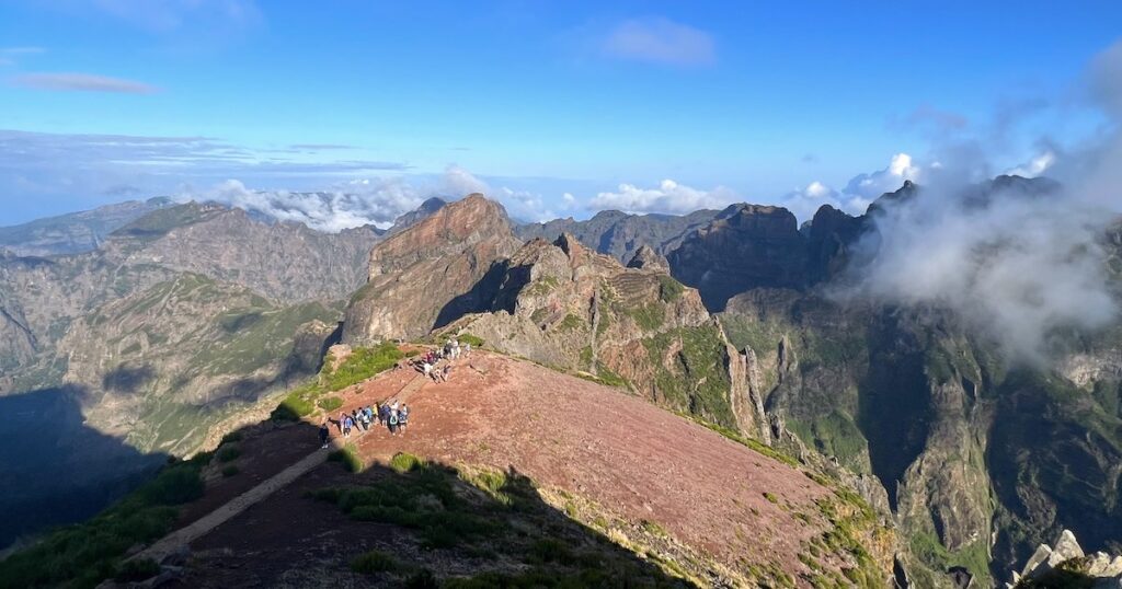 Hikers begin their walk along the PR1 hike in Madeira, surrounded by jagged, green mountains.