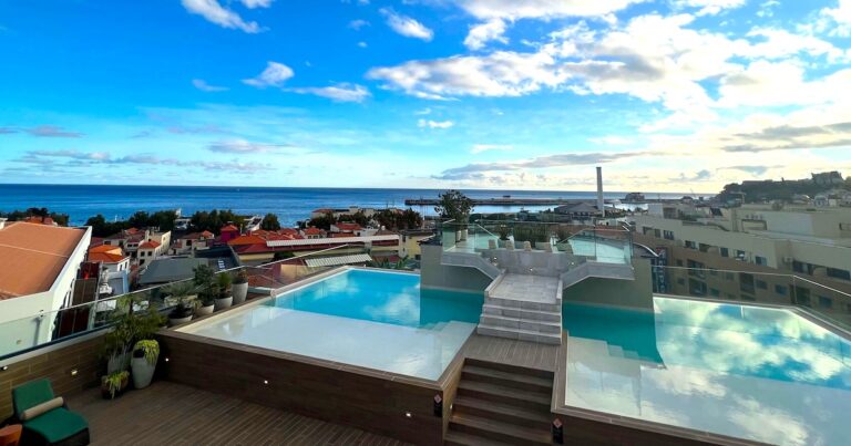 Rooftop infinity pool at Three House in Funchal, overlooking the Atlantic Ocean and Madeira coastline beneath a bright blue sky.
