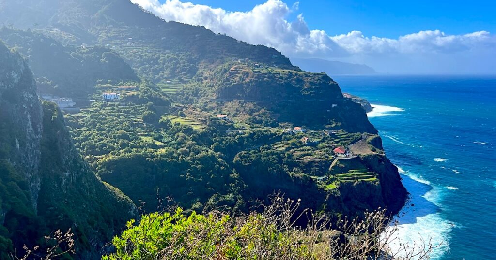 Views from the Caminho Real trail overlooking Madeira’s rugged north coast, with terraced cliffs, scattered houses and waves breaking along the Atlantic shoreline.