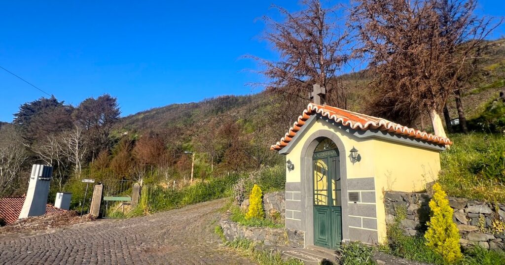 Small roadside chapel on a cobbled mountain lane at Boca da Corrida in Madeira, surrounded by steep green hillsides.