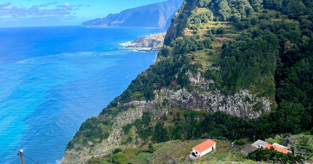 View across Madeira’s rugged coastline with forested cliffs, terraced hillsides and turquoise Atlantic waters.