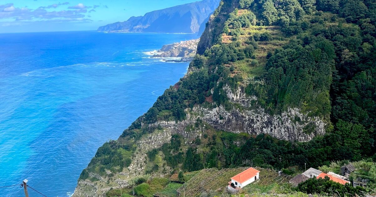 View across Madeira’s rugged coastline with forested cliffs, terraced hillsides and turquoise Atlantic waters.