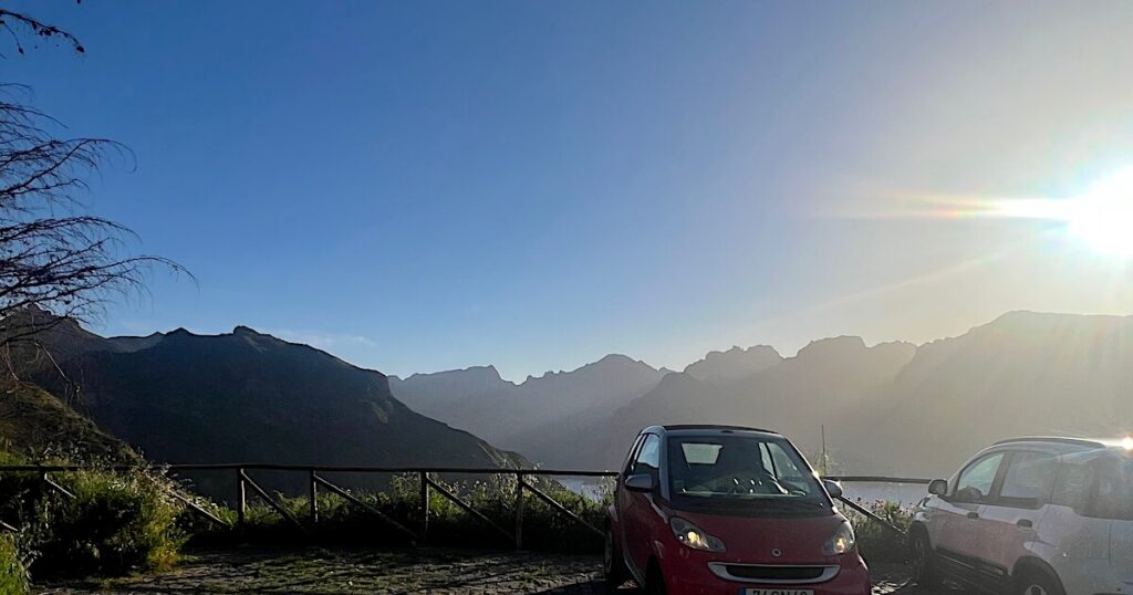 Cars parked at Boca da Corrida viewpoint overlooking Madeira’s peaks and cloud-filled valleys at sunrise.