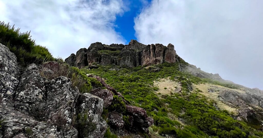 Jagged rock formations and green slopes below Pico Grande, partly shrouded by cloud.