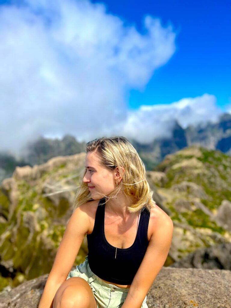 Portrait of a hiker sitting on rocky ground near the Pico Grande summit with cloud and mountain scenery behind.
