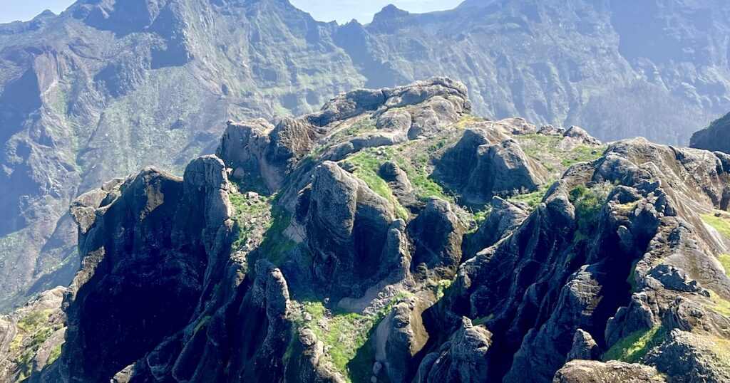 Weathered volcanic rock pinnacles rise from the ridge of Pico Grande, framed by dramatic cliffs and deep mountain ravines in the background.