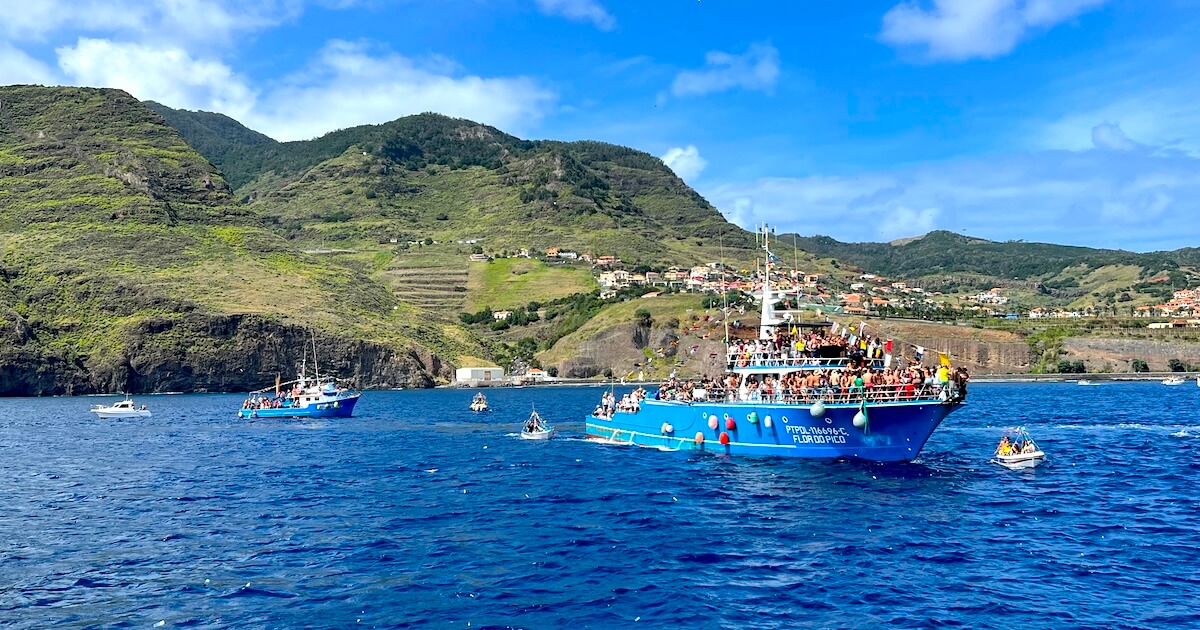 Decorated fishing boats carrying crowds along the coast of Caniçal during the Festa de Nossa Senhora da Piedade.