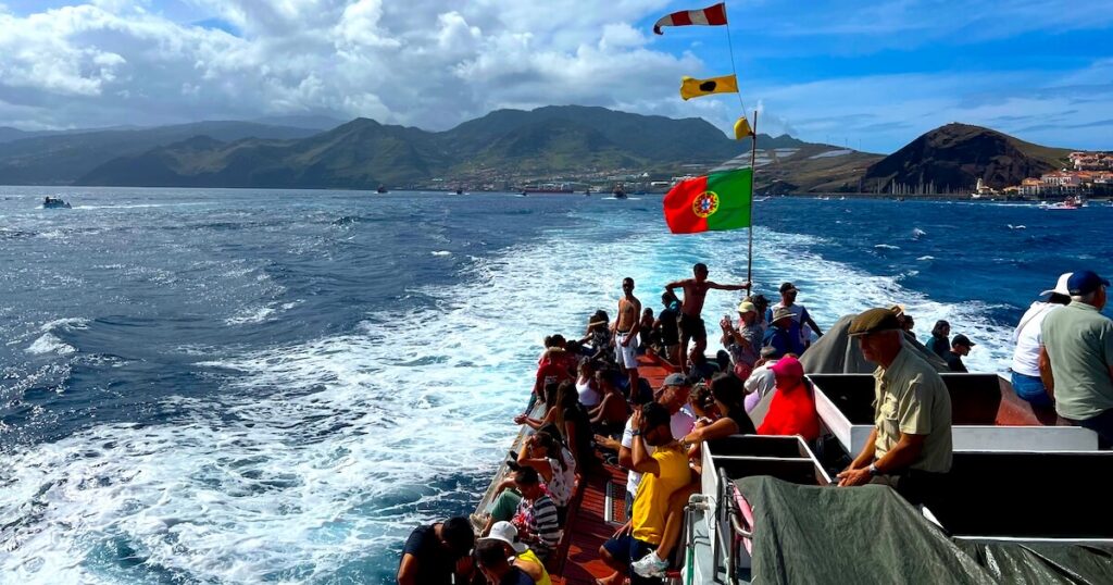 Festival-goers aboard a boat flying the Portuguese flag during the Festa de Nossa Senhora da Piedade procession off Caniçal.
