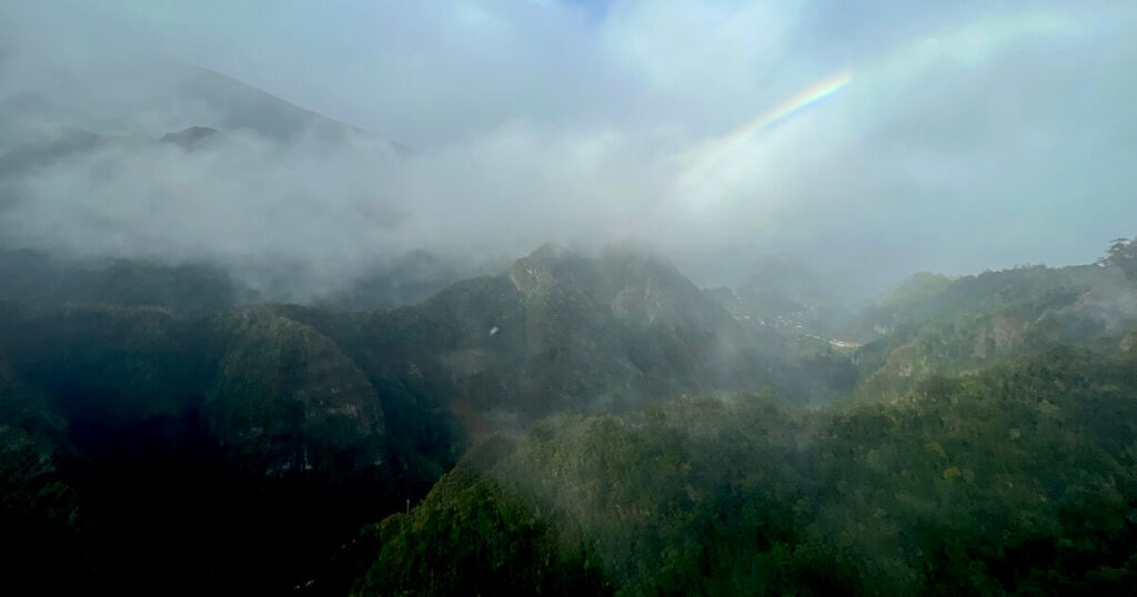 Rainbow appearing above cloud-covered mountain peaks in Madeira.