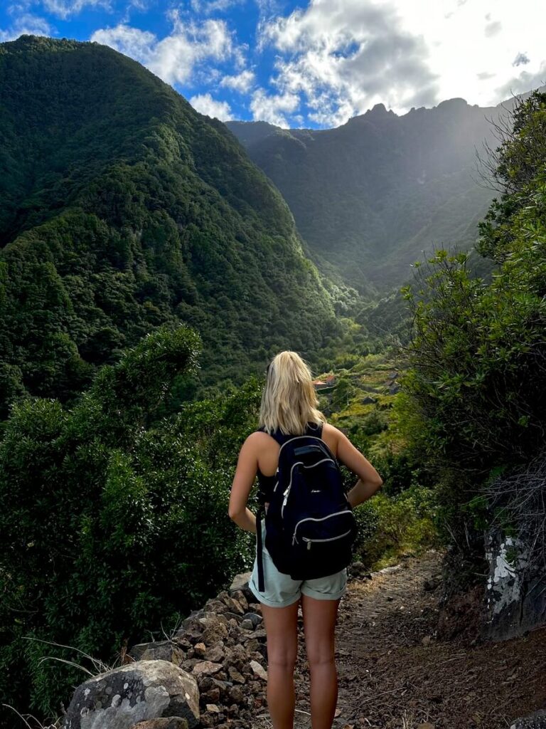 Woman with a backpack overlooking a lush mountain valley from a rocky hiking trail in Madeira in November.