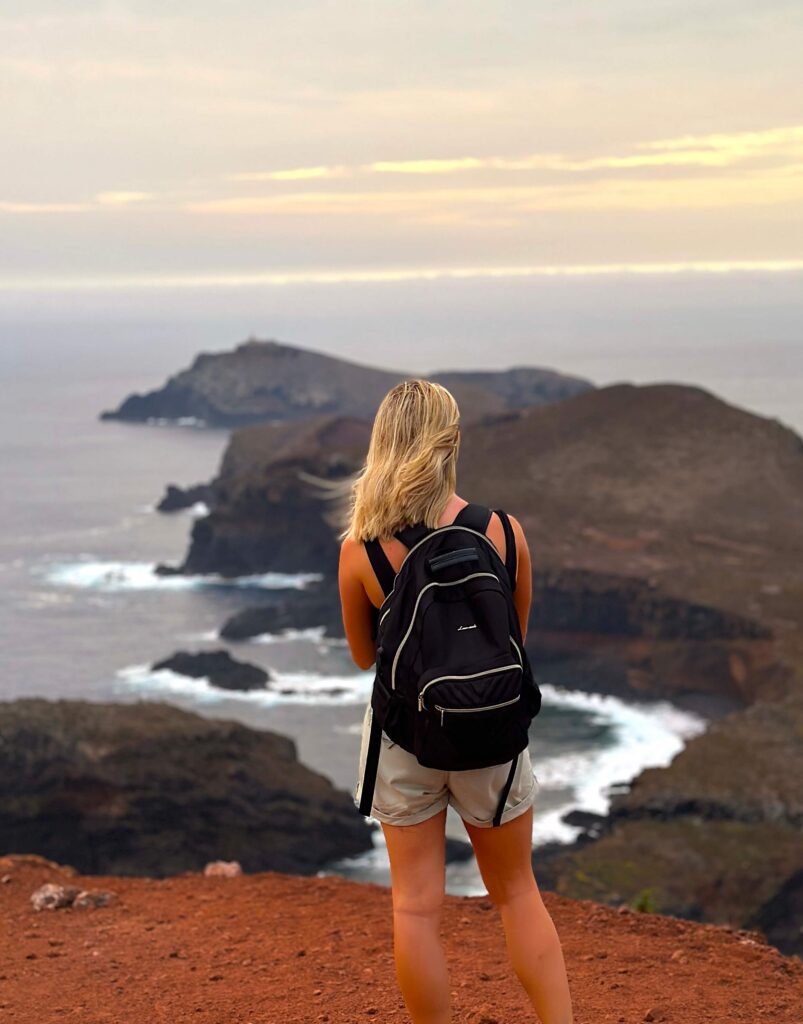 Hiker with a backpack overlooking the rugged Ponta de São Lourenço coastline at sunrise.