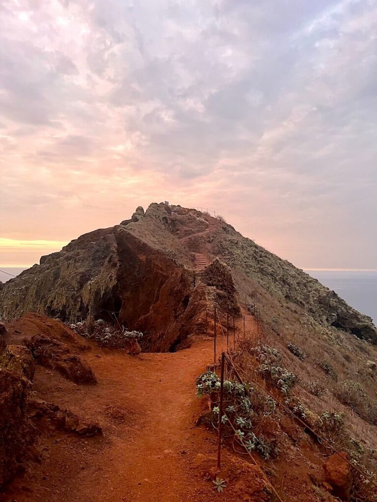 Red-earth PR8 trail curving around a rocky ridge beneath a pink morning sky.