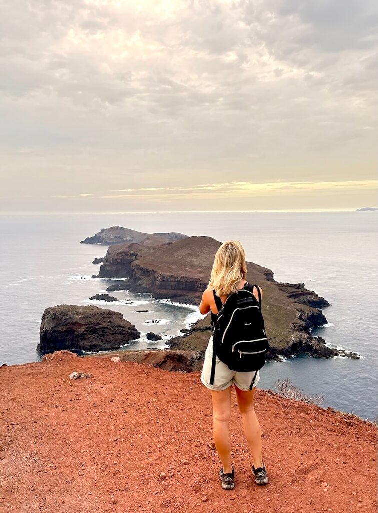 Hiker standing at a red-earth viewpoint overlooking cliffs and offshore islands on Madeira’s PR8 trail.