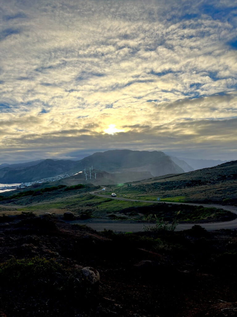 Winding road through open coastal hills near Ponta de São Lourenço beneath clouds lit by the rising sun.